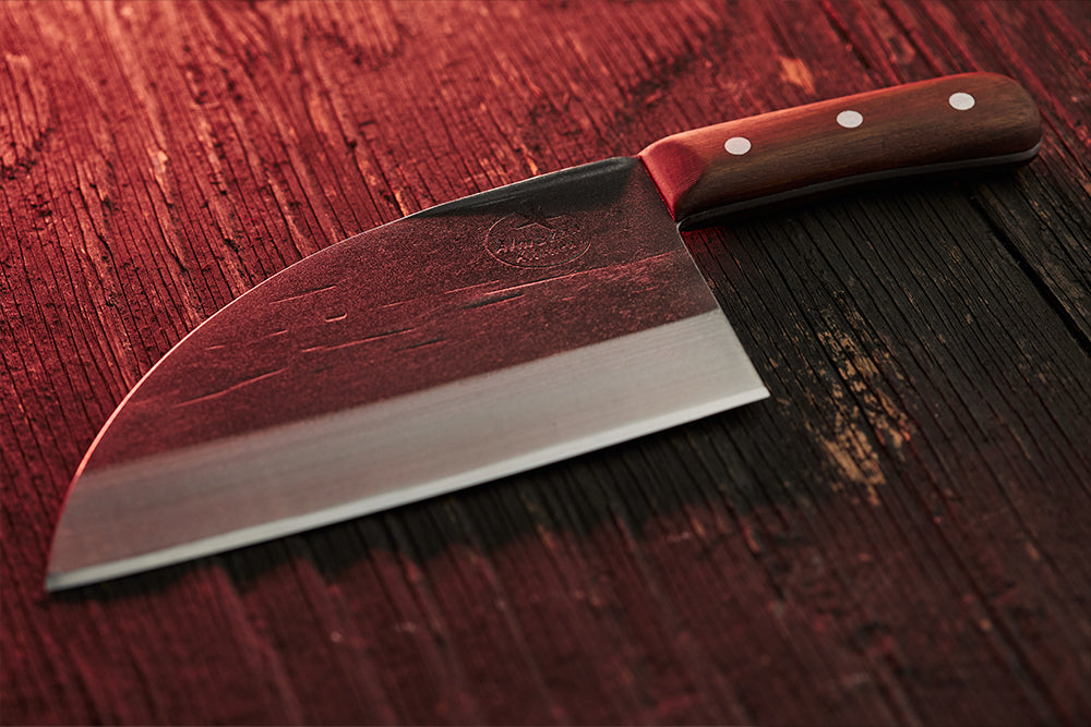 Serbian Chef Knife on a wooden table illuminated by a faint red light.