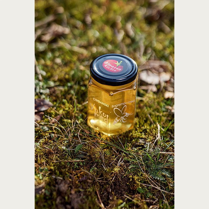 A jar of Almazan Kitchen Organic Honey set on a grassy background.