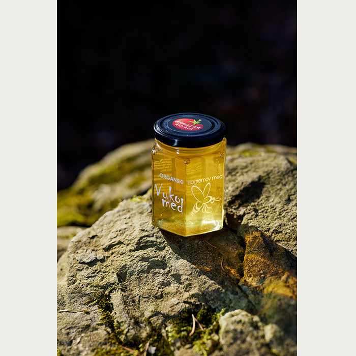 A jar of Almazan Kitchen Organic Honey on a mossy stone with the sun shining on it.