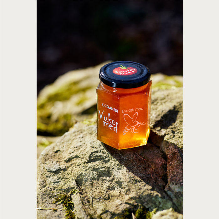 Almazan Kitchen organic meadow honey lit up by rays of sun, with a nature backdrop.