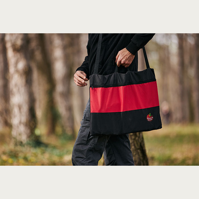 Man carrying a black and red bag in a forest with an Almazan Kitchen logo on it. 