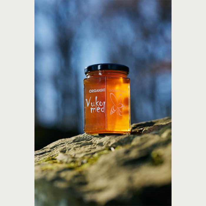 Almazan Kitchen organic meadow honey in a jar, set on a stone with a nature backdrop.