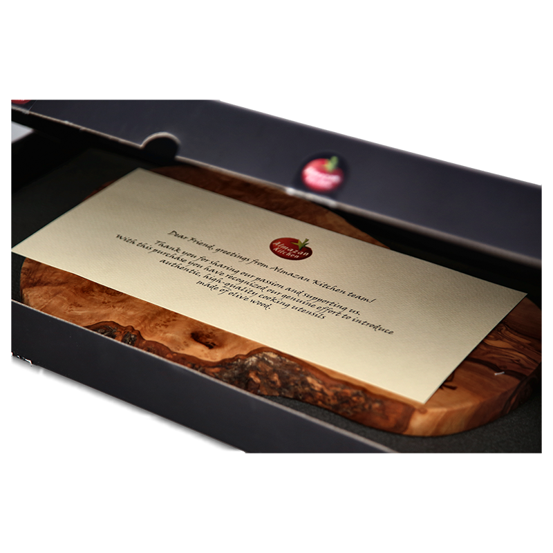 Almazan Kitchen Rustic Olive Wood Board in it's packaging with an accompanying note on a transparent background. 