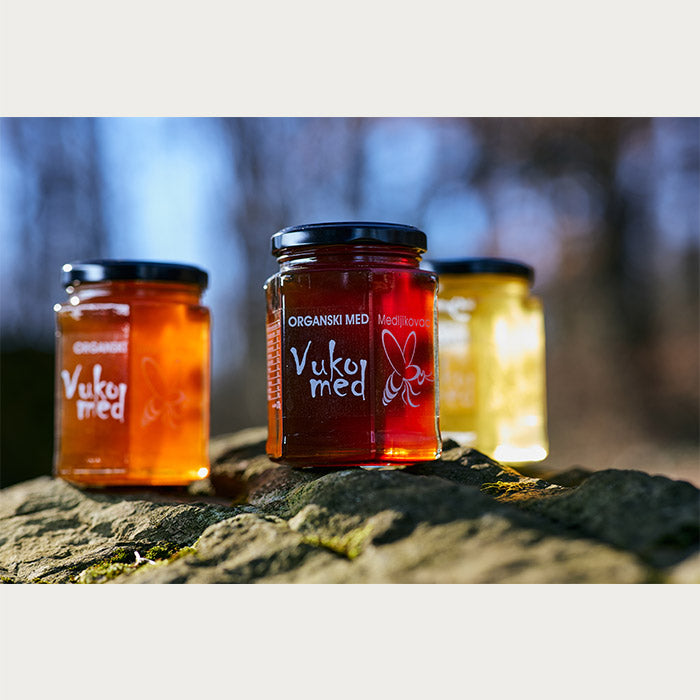 Three jars of Almazan Kitchen organic honey on a stone, with one in front and the other two slightly behind it.