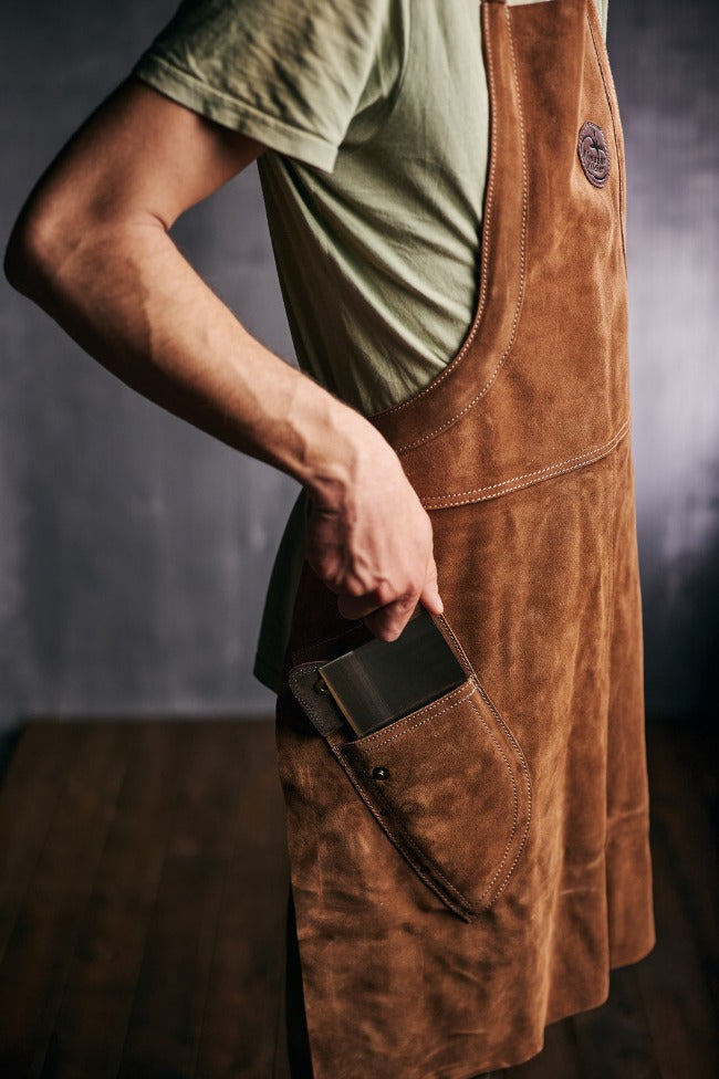 Man pulling out a chef knife from the pocket of a Almazan Kitchen leather apron.