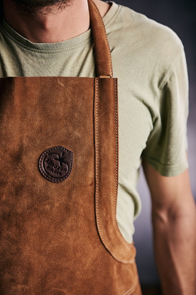 Man wearing a leather apron with the Almazan Kitchen logo displayed on the front.