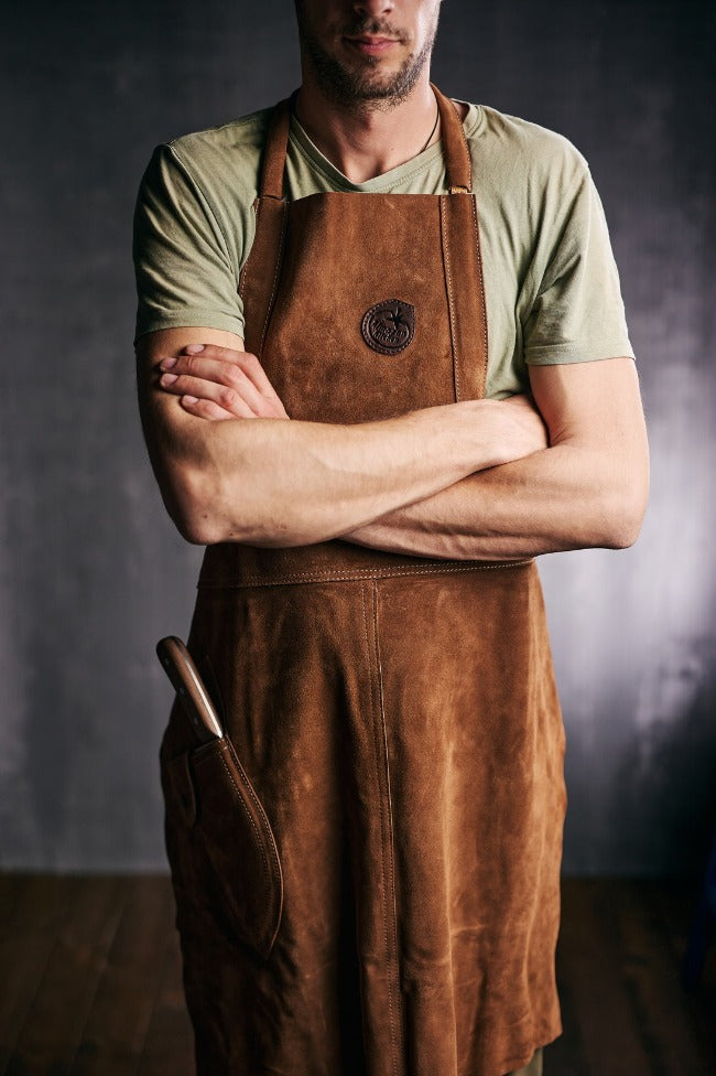 Man with hands crossed over wearing an Almazan Kitchen leather apron.