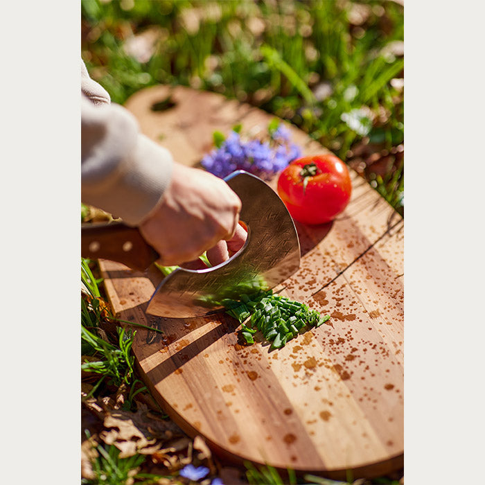 Person in nature, cutting vegetables on a cutting board using a cooking axe.
