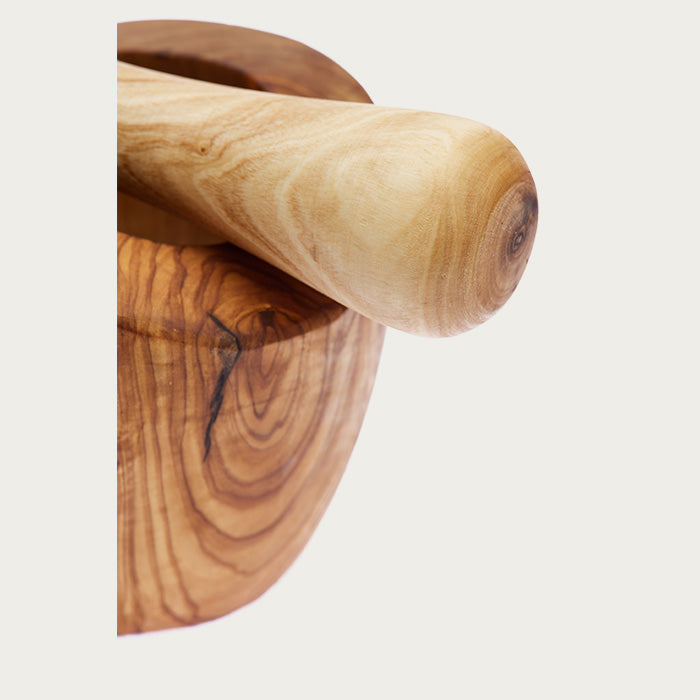 Close up of a wooden pestle set on a mortar with intricate, natural details, on a white background.