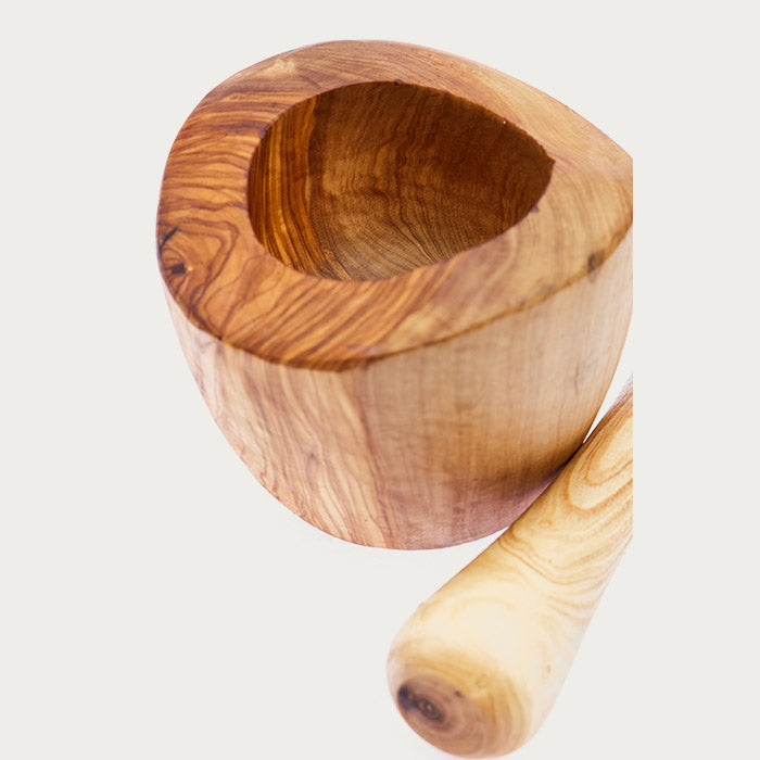 A mortar with intricate wood grains with a wooden pestle next to it on a white background.