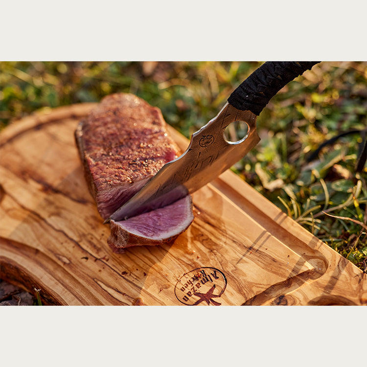 Almazan Kitchen Predator Knife cutting through a piece of meat on a wooden cutting board. 