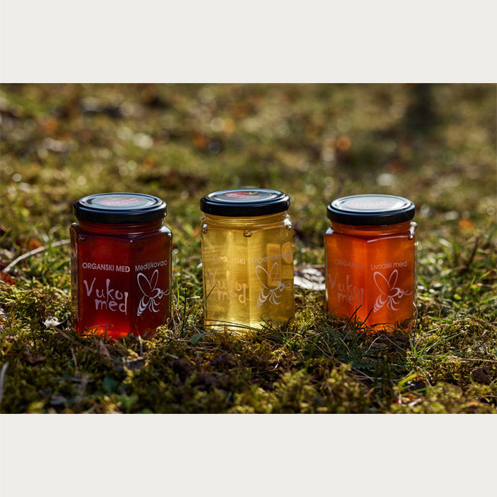 Three jars with different types of Almazan Kitchen organic honey, on a mossy backdrop.