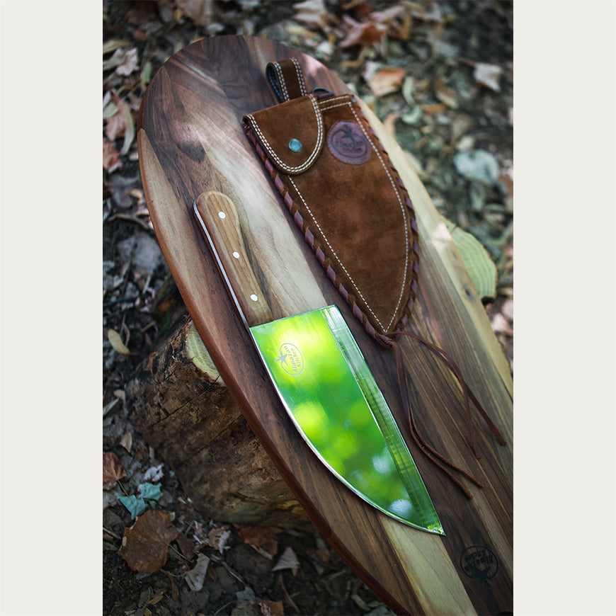 Almazan Kitchen Steak Knife and a brown leather sheath on a wooden cutting board in a forest setting. 