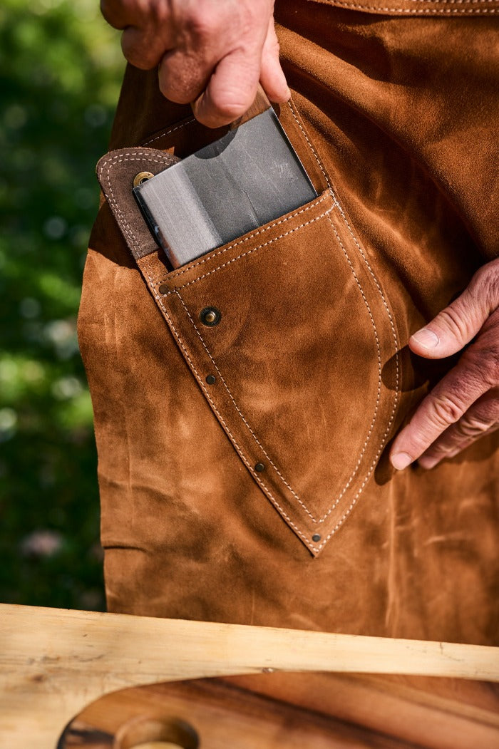 Chef knife being pulled out of a pocket of a leather apron.