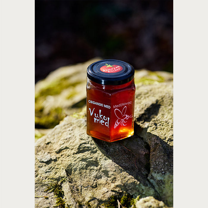 A jar of Almazan Kitchen organic honey on a stone with moss covering it.
