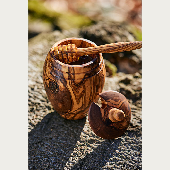 Artisanal olive wood honey jar with honey dipper drizzling honey, in an outdoor setting.