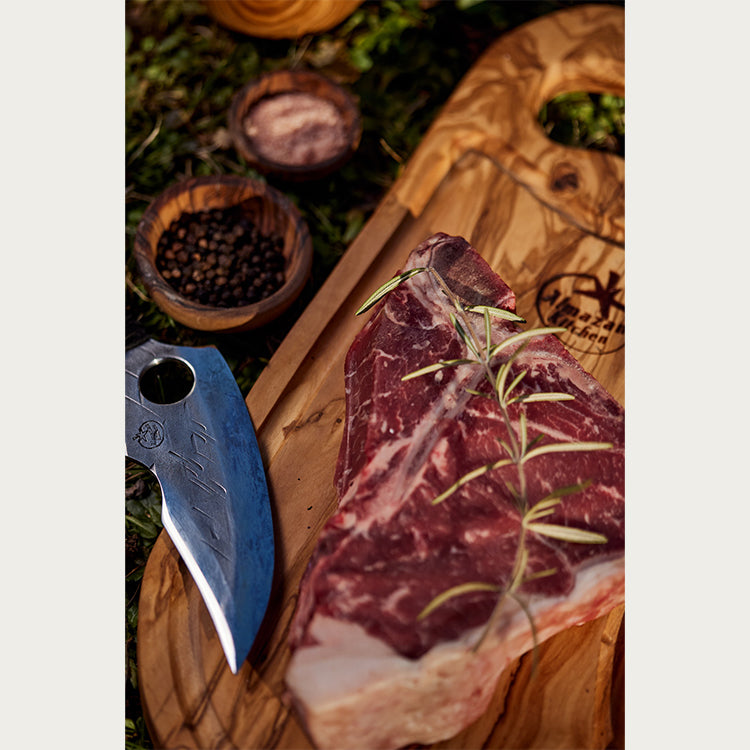 A piece of steak on a cutting board with seasoning and a predator knife next to it.