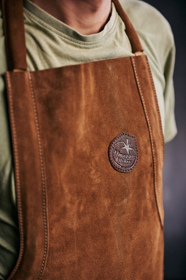 Man wearing a leather apron with the Almazan Kitchen logo in focus.