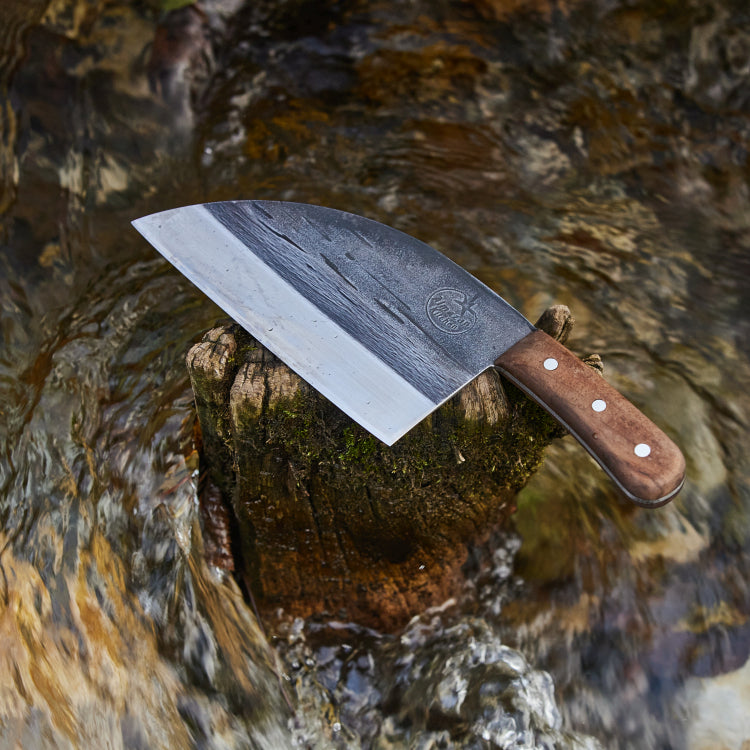 Almazan Kitchen Serbian Chef Knife on a stone in the middle of a creek.