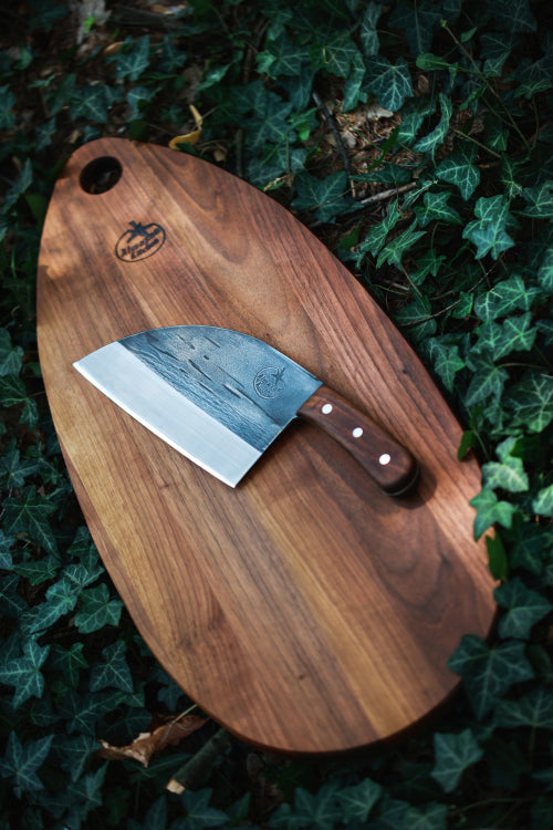 Cutting board in leaves with a Almazan Kitchen Serbian Chef Knife on it. 