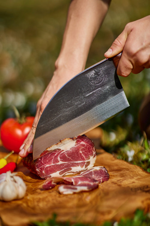 Person cutting meat in nature, with an Almazan Kitchen Serbian Chef Knife.
