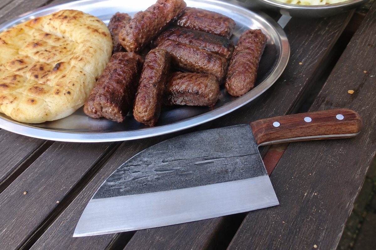 Serbian chef knife beside grilled meat and flatbread